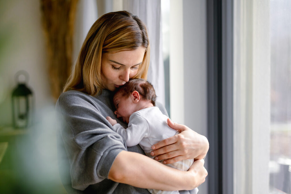 Woman gently holding a newborn baby near a window at home